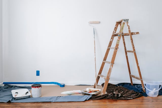 ladder and pain cans and blue painting tape next to a white wall